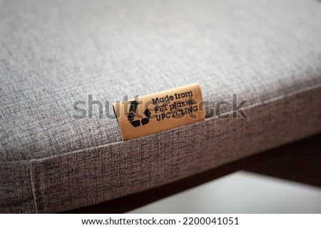 "PET Plastic upcycling" product label tag on the sofa seat fabric material part. Sign and symbol object photo, selective focus.