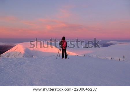 Silhouette of woman photographer with tripod on Mount Sniezka at sunrise in beautiful winter scenery. Karkonosze Mountains (Giant Mountains), Poland
