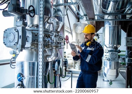 Heating plant interior with pipes and valves and factory worker controlling process of boiling.