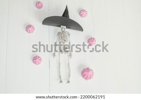 soft pink pumpkins on a light background and a toy skeleton in a witch hat , a place for text , an abstract Halloween concept