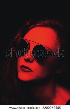 Style, make-up and fashion concept. Beautiful woman with round retro sunglasses and long wavy hair close-up studio portrait. Model looking aside the camera. toned image with red and black colors