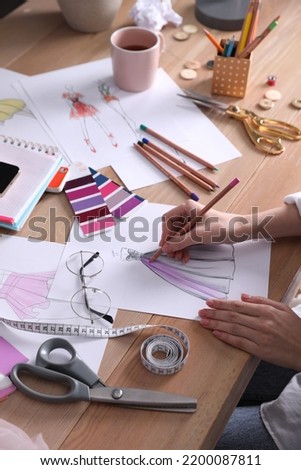 Fashion designer drawing sketch at wooden table, closeup