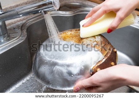 Woman's hand washing half of a burnt frying pan Royalty-Free Stock Photo #2200095267