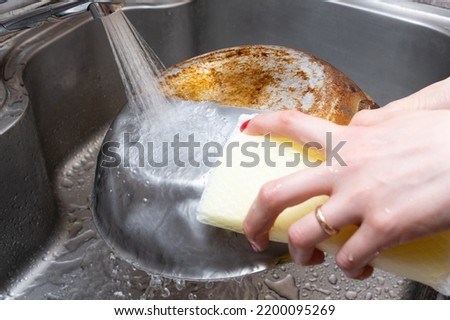 Woman's hand washing half of a burnt frying pan Royalty-Free Stock Photo #2200095269