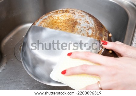 Woman's hand washing only half of a burnt frying pan Royalty-Free Stock Photo #2200096319