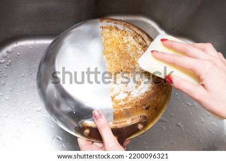 Woman's hand washing only half of a burnt frying pan Royalty-Free Stock Photo #2200096321