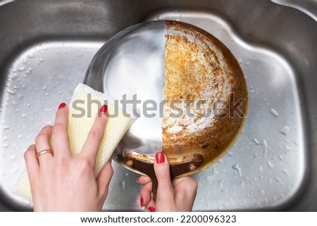 Woman's hand washing only half of a burnt frying pan Royalty-Free Stock Photo #2200096323
