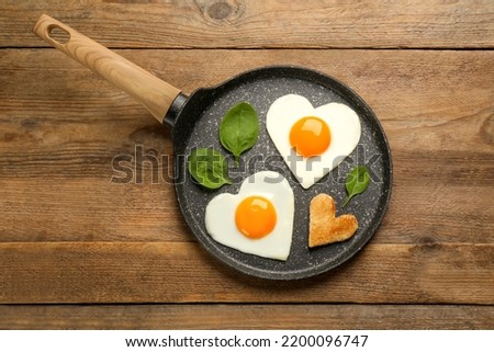 Heart shaped fried eggs with toast in frying pan on wooden table, top view