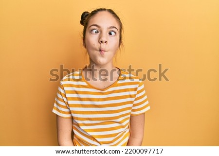 Beautiful brunette little girl wearing casual striped t shirt making fish face with lips, crazy and comical gesture. funny expression. 