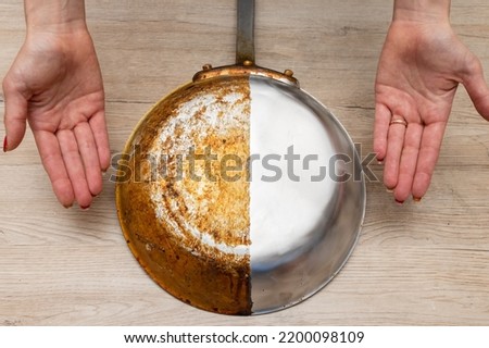 A woman's hand presenting a frying pan that is half burnt and half polished Royalty-Free Stock Photo #2200098109