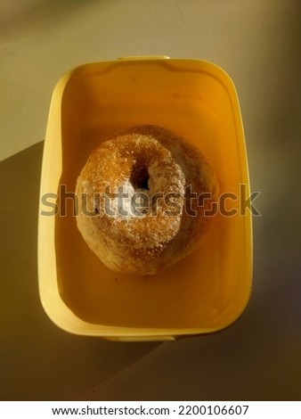 One donut coated with powdered sugar on a plastic bowl