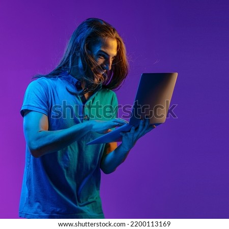 A nice emotional guy holds a laptop in his hands and looks at the screen with surprise. colored neon light