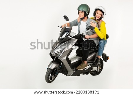 young attractive couple riding an electric motorbike scooter happy having fun together, stylish hipster man and woman isolated on white studio background wearing safety helmets speed action Royalty-Free Stock Photo #2200138191