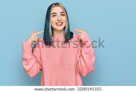 Young modern girl wearing pink wool winter sweater smiling cheerful showing and pointing with fingers teeth and mouth. dental health concept. 