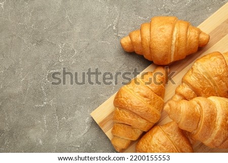 Freshly baked croissants on wooden cutting board on grey background. Top view