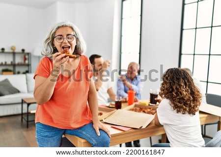 Group of middle age people smiling happy eating italian pizza sitting on the table at home