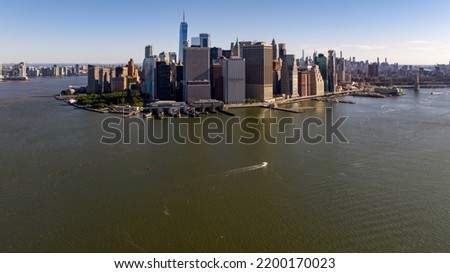 An aerial view of lower Manhattan, NY on a sunny day with no clouds. The East River is calm.