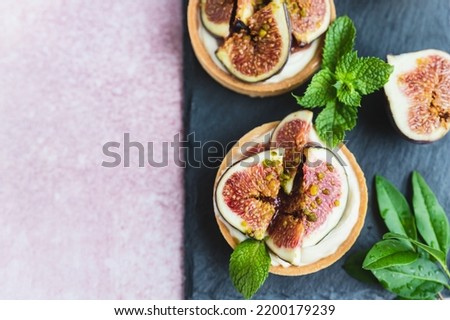 Tartlets pastry with white cream, topped with figs and pistachio on pink background. Cooking concept. Healthy dessert. Top view.