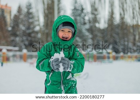 the boy carries snow in his hands. Winter Games. a little boy plays outside in the winter. boy smiling