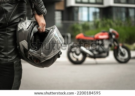 Biker walks to motorcycle holding helmet in hand Royalty-Free Stock Photo #2200184595