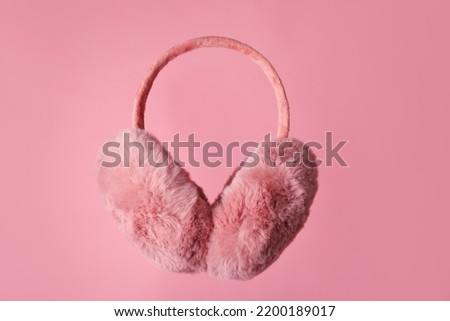Fluffy earmuffs on pink background. Stylish winter accessory