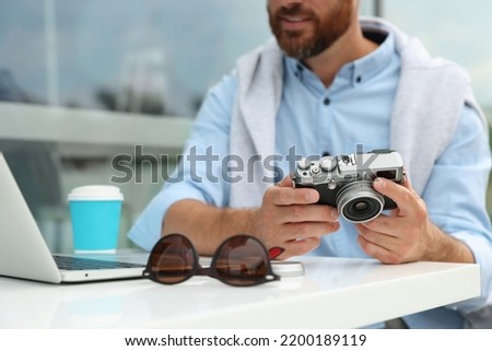 Man with camera, coffee and laptop in outdoor cafe, closeup. Interesting hobby