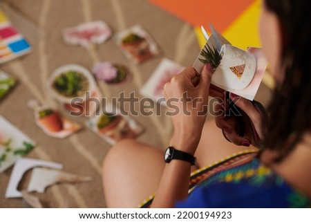 Close-up image of woman cutting out pictures of plants for collage
