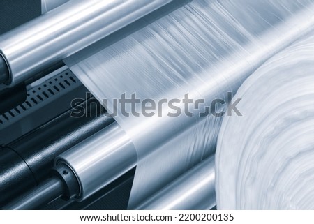 Automatic polyethylene plastic bag production machine with lighting effect. Close-up of the roller of the plastic bag production machine in the light blue scene. product packaging concept Royalty-Free Stock Photo #2200200135