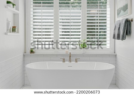 Modern luxury soaking tub with brass faucet interior design staged with plantation shutters Royalty-Free Stock Photo #2200206073