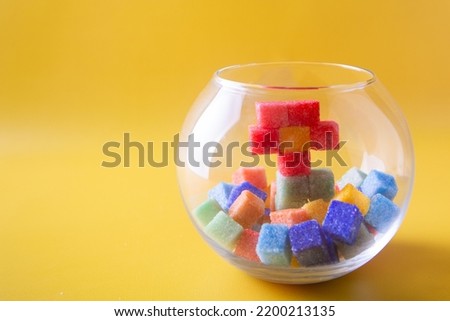 Pixel art flower made of red, green sugarcubes stay inside small glass aquarium near different color sugar cubes on yellow background. Copy space for your text