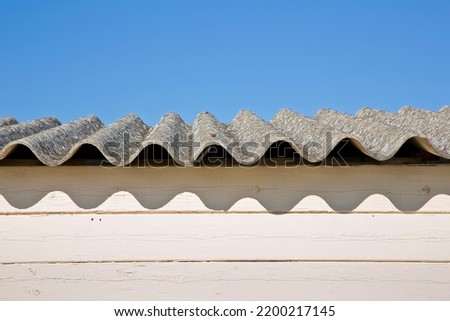 Old aged dangerous roof made of corrugated asbestos panels - one of the most dangerous materials in buildings and construction industry so-called hidden killer. Royalty-Free Stock Photo #2200217145