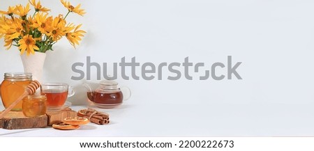 Autumn banner with hot tea in a glass cup, honey and spices on the background of seasonal flowers and leaves, space for text, cozy warm autumn concept, hygge style,