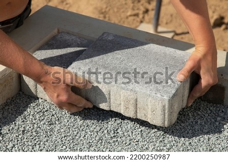 craftsman lays down the paving stones in layers. Laying gray concrete paving slabs in the courtyard of the house on a sandy foundation.