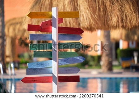 Summer recreation in tropical country. Colourful signboard pointing direction to outdoor pool, straw shadow parasols on sunny day