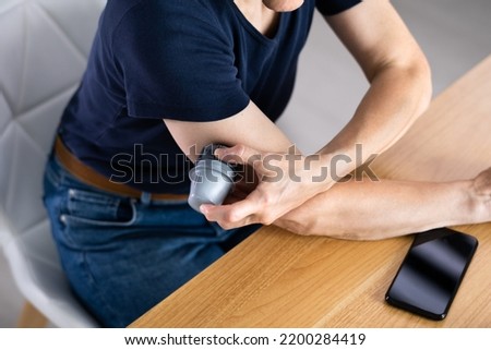 Woman Installing Continuous Glucose Level Monitor On Her Arm Royalty-Free Stock Photo #2200284419