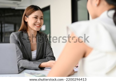 Beautiful and cheerful Asian female business consultant or insurance agent meets with her female client in the office. Royalty-Free Stock Photo #2200296413