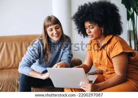 Young businesswomen having a discussion while using a laptop together. Two female entrepreneurs working as a team in a modern workplace. Royalty-Free Stock Photo #2200297087