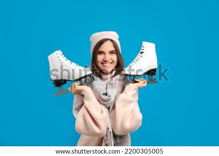 Happy woman with ice skates on light blue background