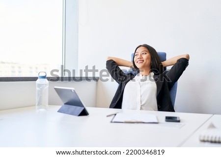 Relaxed young woman with her hands behind her head takes a rest in the office Royalty-Free Stock Photo #2200346819