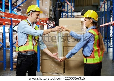 factory workers or warehouser wrapping stretch film parcel on pallet covered cardboard boxed in warehouse storage