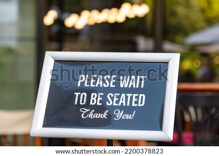 Please wait to be seated sign standing at the front of a restaurant. Sidewalk cafe hostess stand with message signboard for clients