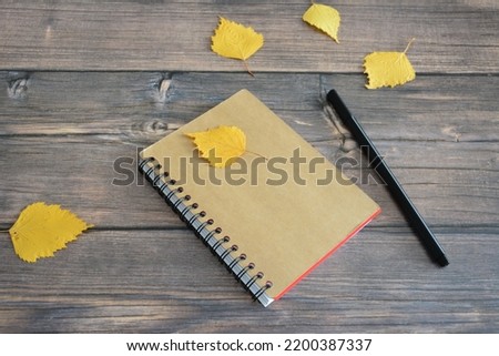 pocket notepad on the wooden background with pencil and dry autumn leaves