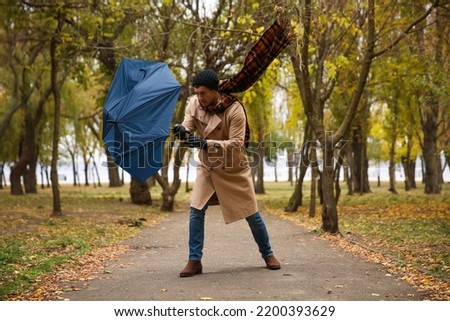 Man with blue umbrella caught in gust of wind outdoors Royalty-Free Stock Photo #2200393629