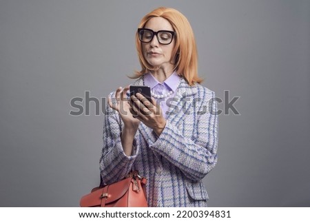 Funny snobbish lady using her smartphone and chatting, isolated on gray background Royalty-Free Stock Photo #2200394831