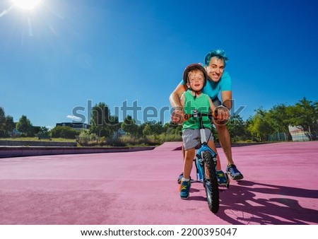 Father with blue hair help little boy learn riding a bicycle in the park
