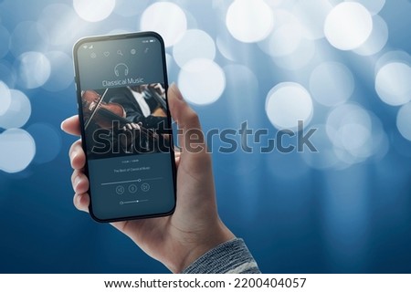 User holding a smartphone and listening to classical music online, blank copy space