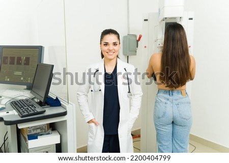 Professional female doctor smiling while doing a mammogram to a young woman to prevent breast cancer at the medical imaging lab