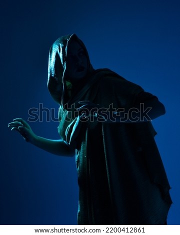 Close up portrait of beautiful woman model wearing elegant black dress hooded cloak,, posing against a studio background with fantasy inspired arm gestures, multi coloured creative lighting.