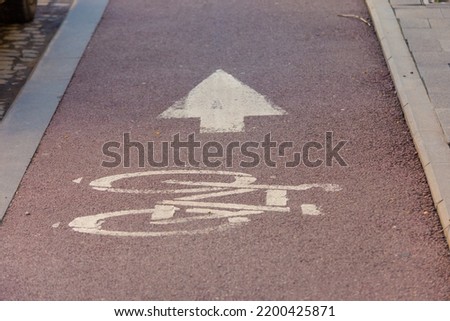 Bicycle lane road mark on red asphalt with a white arrow next to a paved sidewalk
