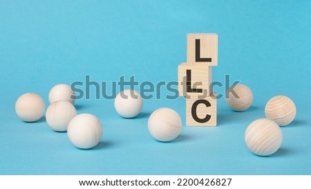 LLC text on wooden block with blue background. Limited Liability Company